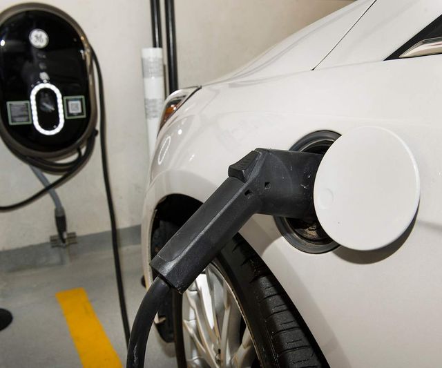 Weißes Elektroauto lädt in einem Parkhaus, der Stecker steckt im Fahrzeug, die Wallbox hängt an der Wand
