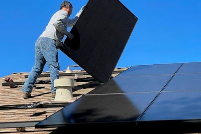 Monteur trägt ein Solarmodul über ein Dach