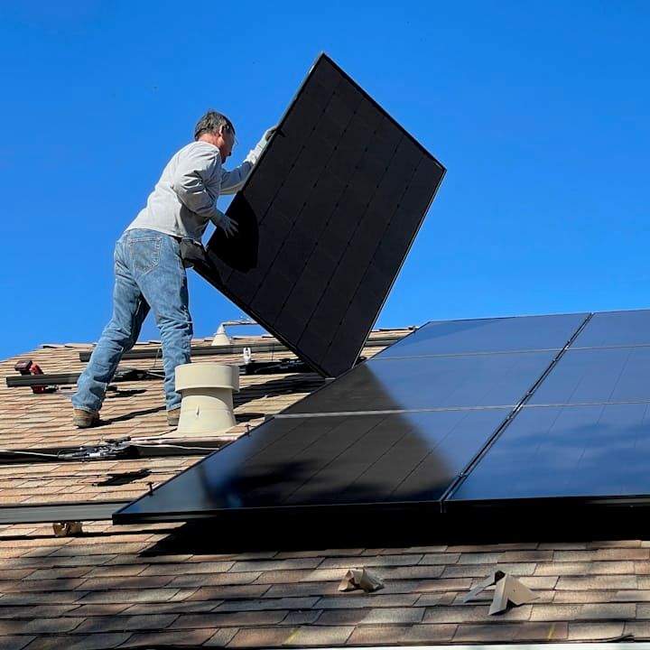 Monteur trägt ein Solarmodul über ein Dach