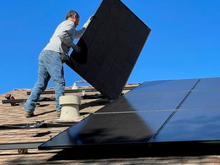 Monteur trägt ein Solarmodul über ein Satteldach