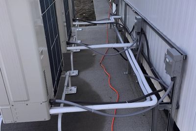 Außeneinheiten einer Wärmepumpe von hinten, davor gedämmte Leitungen und Anschlusskästen an der Wand