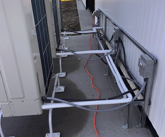Außeneinheiten einer Wärmepumpe von hinten, davor gedämmte Leitungen und Anschlusskästen an der Wand