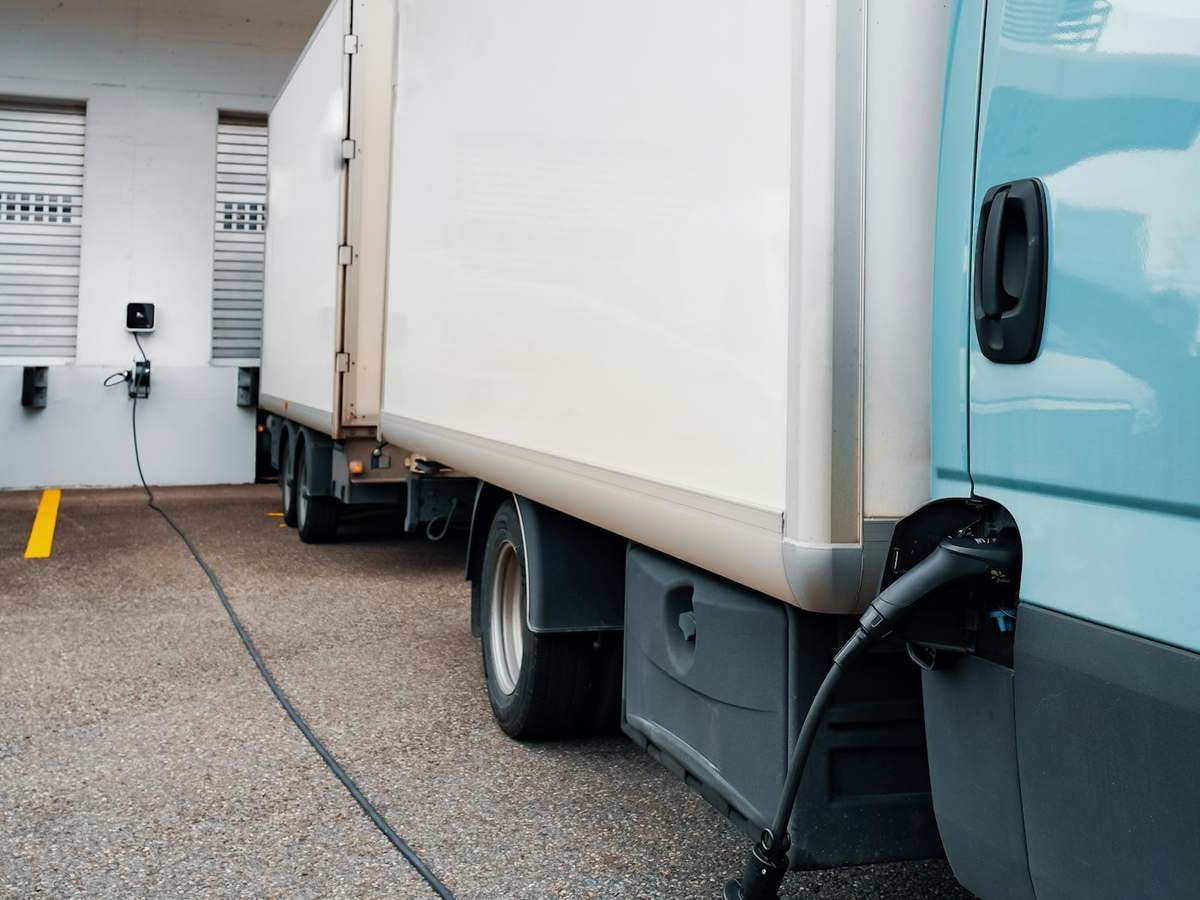 Elektrischer Lieferwagen lädt über ein Kabel an einer Wallbox an der Hallenwand